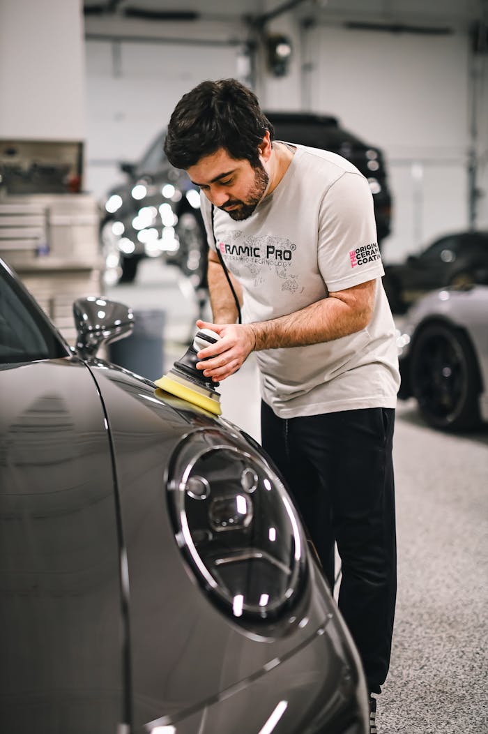 Man carefully polishing a sleek sports car in a well-lit garage, focused on detailing.
